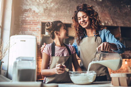 Attractive young woman and her little cute daughter are cooking on kitchen. Having fun together while making cakes and cookies.の写真素材