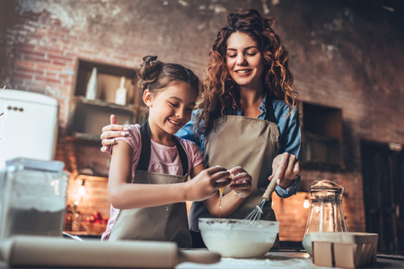 Attractive young woman and her little cute daughter are cooking on kitchen. Having fun together while making cakes and cookies.の写真素材