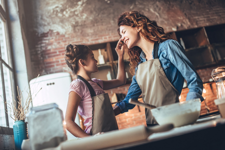 Attractive young woman and her little cute daughter are cooking on kitchen. Having fun together while making cakes and cookies.の写真素材