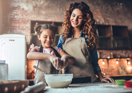 Attractive young woman and her little cute daughter are cooking on kitchen. Having fun together while making cakes and cookies.の写真素材