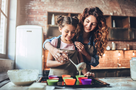 Attractive young woman and her little cute daughter are cooking on kitchen. Having fun together while making cakes and cookies.の写真素材