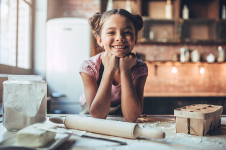 Little cute girl is cooking on kitchen. Having fun while making cakes and cookies. Smiling and looking at camera.の写真素材
