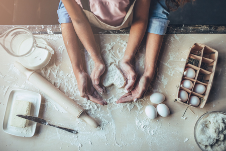 Cropped image of attractive young woman and her little cute daughter are cooking on kitchen. Having fun together while making cakes and cookies. Top view of mom with daughter making dough heart.の写真素材