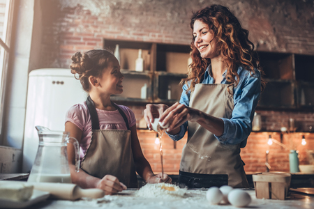 Attractive young woman and her little cute daughter are cooking on kitchen. Having fun together while making cakes and cookies. Doing dough for pasta.の写真素材