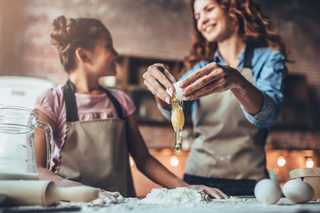 Attractive young woman and her little cute daughter are cooking on kitchen. Having fun together while making cakes and cookies. Doing dough for pasta.の写真素材