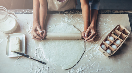 Cropped image of attractive young woman and her little cute daughter are cooking on kitchen. Having fun together while making cakes and cookies. Top view of mom with daughter making dough.の写真素材