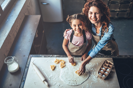 Top view of attractive young woman and her little cute daughter are cooking on kitchen. Having fun together while making cakes and cookies.の写真素材