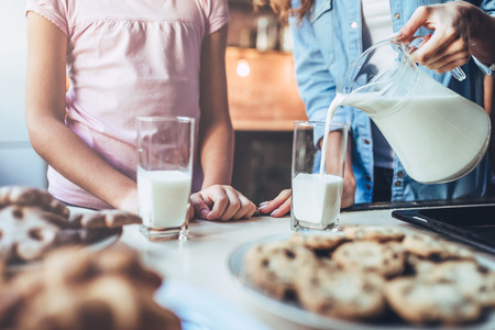 Cropped image of attractive young woman and her little cute daughter are eating cakes and cookies on kitchen and drinking milk. Having fun together while enjoying 
freshly baked pastries.の写真素材