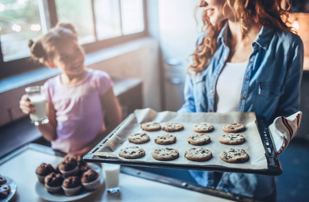 Cropped image of attractive young woman and her little cute daughter are eating cakes and cookies on kitchen and drinking milk. Having fun together while enjoying 
freshly baked pastries.の写真素材
