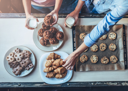 Cropped image of attractive young woman and her little cute daughter are eating cakes and cookies on kitchen and drinking milk. Having fun together while enjoying
freshly baked pastries. Top view.の写真素材
