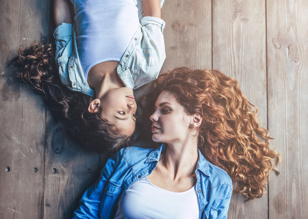 Beautiful curly woman and little pretty girl at home. Top view of mother with daughter are lying on the wooden floor.の写真素材