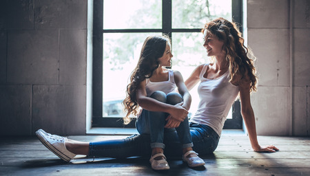 Beautiful curly woman and her little pretty daughter at home. Having fun and enjoying being together.の写真素材