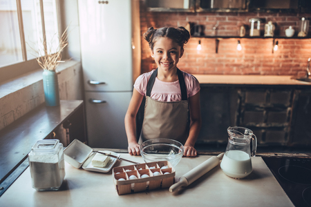 Little cute girl is cooking on kitchen. Having fun while making cakes and cookies. Smiling and looking at camera.の写真素材