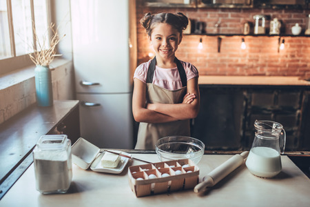 Little cute girl is cooking on kitchen. Having fun while making cakes and cookies. Smiling and looking at camera.の写真素材
