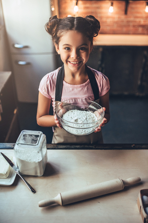 Little cute girl is cooking on kitchen. Having fun while making cakes and cookies. Smiling and looking at camera.の写真素材