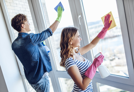 Young happy couple is washing windows while doing cleaning at home.の写真素材