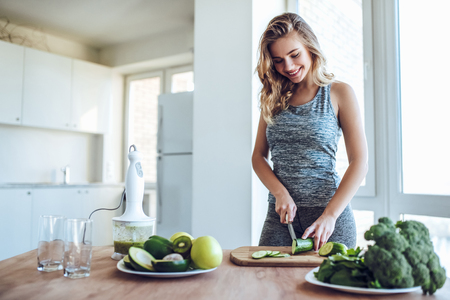 Sporty young woman is preparing healthy food on light kitchen. Green healthy food concept.の写真素材