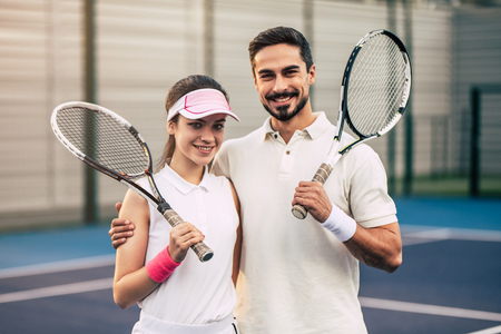 Young couple on tennis court. Handsome man and attractive woman are playing tennis. Hugging, smiling and looking at camera.の写真素材