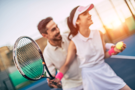 Young couple on tennis court. Handsome man is teaching attractive woman how to play tennis.の写真素材