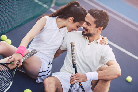 Young couple is sitting on tennis court. Handsome man and attractive woman are playing tennis.の写真素材