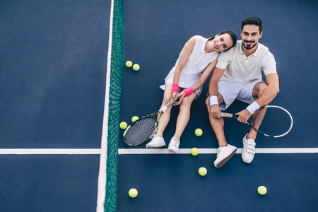 Top view of young couple is sitting on tennis court. Handsome man and attractive woman are playing tennis.の写真素材