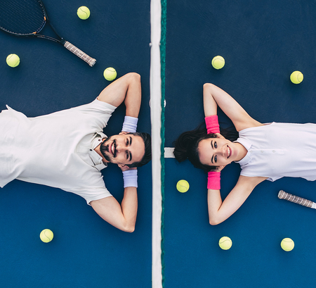 Top view of young couple is lying on tennis court. Handsome man and attractive woman are playing tennis.の写真素材
