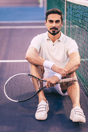 Handsome man is sitting on tennis court. Young male tennis player.の写真素材