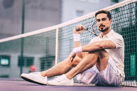 Handsome man is sitting on tennis court. Young male tennis player.の写真素材