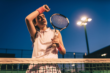 Sport young woman on tennis court in the evening. Female tennis player.の写真素材