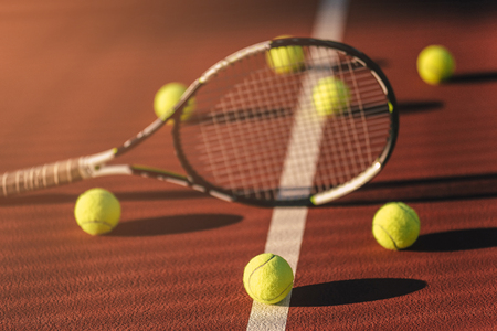 Balls and racket are lying on brown tennis court.の写真素材