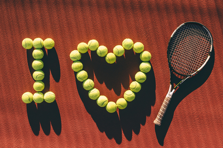 Balls and racket are lying on brown tennis court. I love tennis.の写真素材