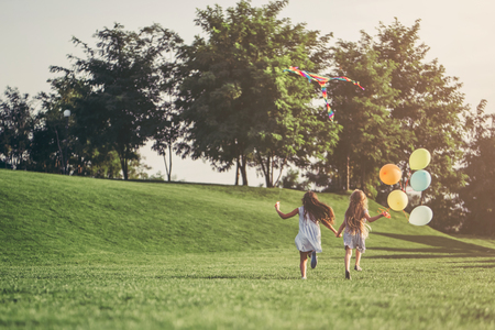 Little pretty girls having fun outdoor. Two cute girls are running on green grass with air balloons. Best friendsの写真素材