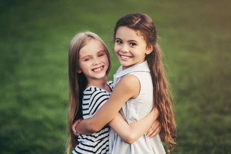 Little pretty girls having fun outdoor. Two cute girls are standing on green grass and hugging. Best friends.の写真素材