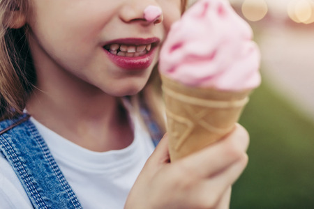 Cropped image of little pretty girl is having fun outdoor. Standing on green grass and with ice...