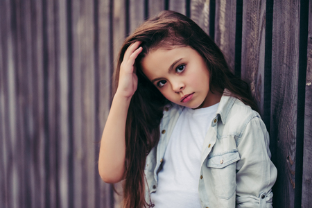 Little pretty girl outdoor. Fashionable child posing on the background of wooden fence.の写真素材