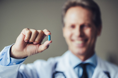 Portrait of experienced senior doctor with stethoscope in clinic. Holding pill in hand.の写真素材