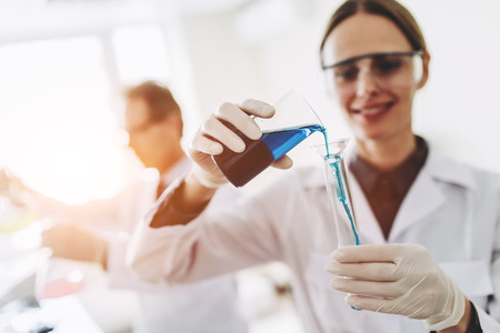 Two scientists are working in laboratory. Young female researcher and her senior supervisor are doing investigations with test tubes.の写真素材