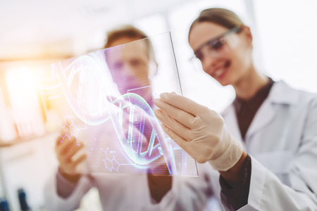 Two scientists are working in laboratory. Young female researcher and her senior supervisor are doing investigations. Working with glass tablet.の写真素材
