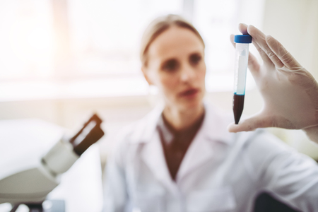 Experienced female scientist is working in laboratory. Doing investigations with microscope and test tubes.の写真素材