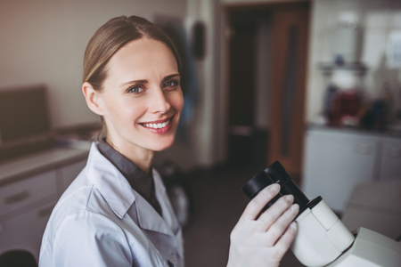 Experienced female scientist is working in laboratory. Doing investigations with microscope.の写真素材