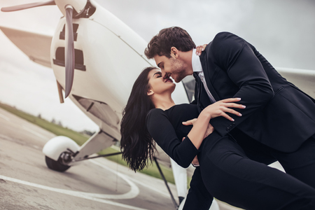 Beautiful young stylish couple  in official clothes near private plane. Hugging and kissing in airport in front of airplane.の写真素材