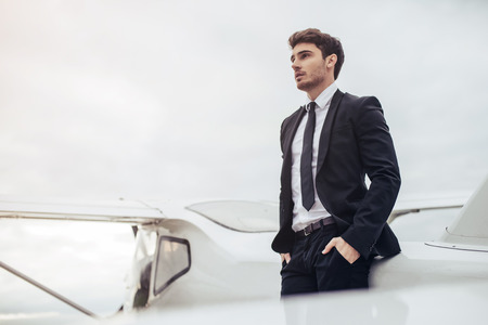 Young handsome businessman is standing near private plane. Confident and successful man in airport.