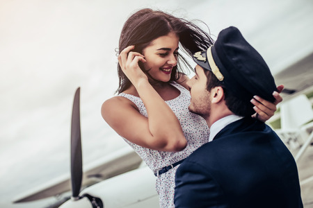 Young handsome man pilot in uniform is standing near small private plane with his beautiful young...