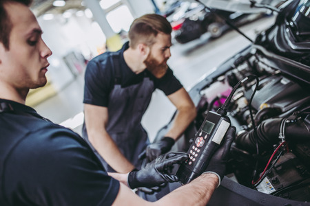 Two handsome mechanics in uniform are working in auto service. Car repair and maintenance....
