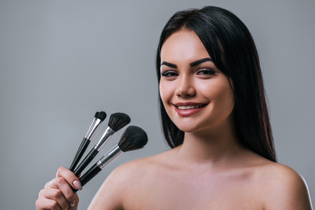 Portrait of attractive young woman with makeup brushes on grey background. Women careの写真素材