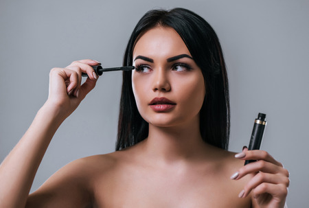 Portrait of attractive young woman using mascara on grey background. Women careの写真素材