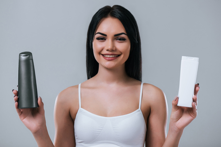 Portrait of attractive young woman with two shampoos on grey background. Making choice. Women careの写真素材