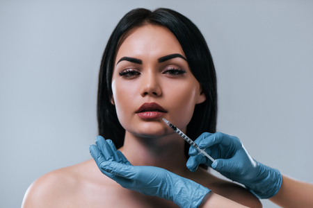 Portrait of attractive young woman making cosmetic injections on grey background. Women face care. Cosmetology concept.の写真素材