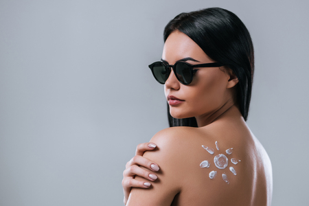 Portrait of attractive young woman in sunglasses with sunscreen is standing on grey background. Women care and body protectionの写真素材