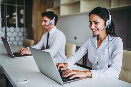 How can I help you? Beautiful call center workers in headphones are working at modern office.の写真素材